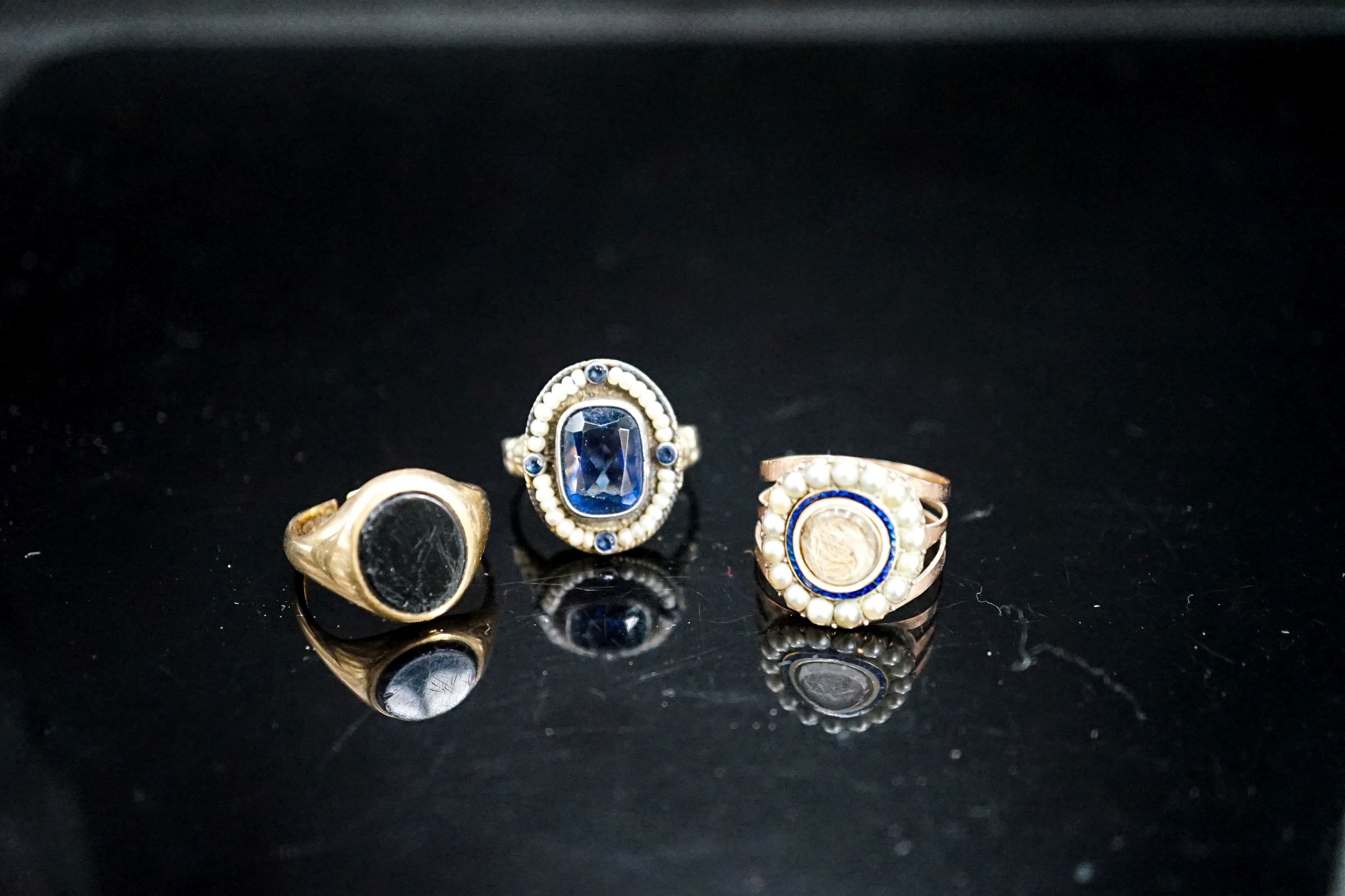 A 19th century yellow metal, two colour enamel and seed pearl set mourning ring, with hair beneath a glazed panel, size N, a 19th century Austro-Hungarian white metal and blue paste ring and a later 9ct gold signet ring(